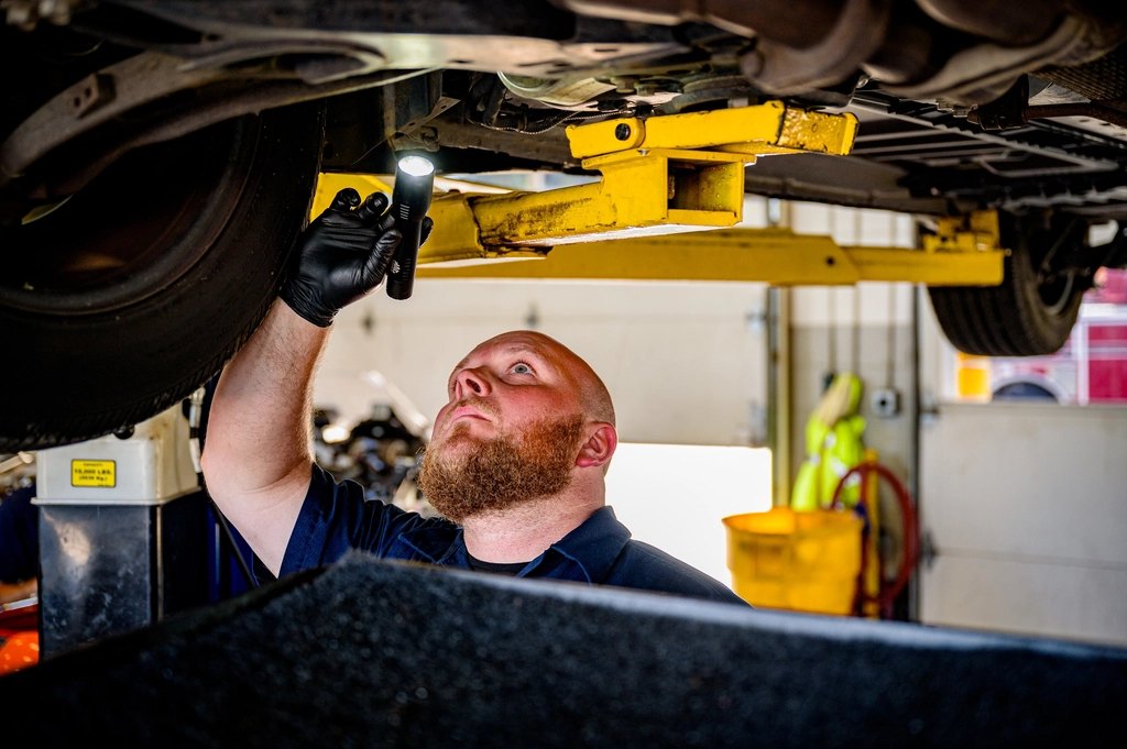 Mechanik prosvěcuje podvozek vozu na zvedáku při servisní prohlídce